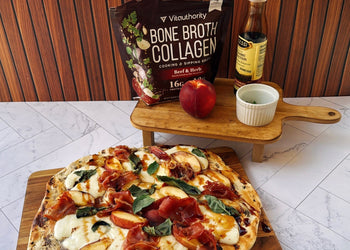 Pizza resting on a cutting board with peach, balsamic vinegar and bone broth collagen in background.