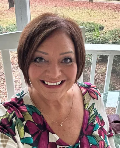 Woman taking a selfie with short brown hair wearing a colorful floral top on a porch