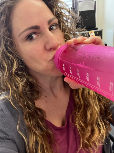 Woman taking a selfie while drinking from a pink water bottle 